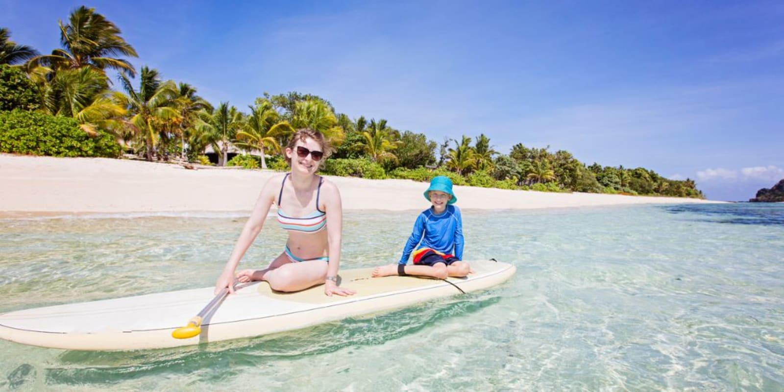 A family sitting on a paddle board in the water just off the beach