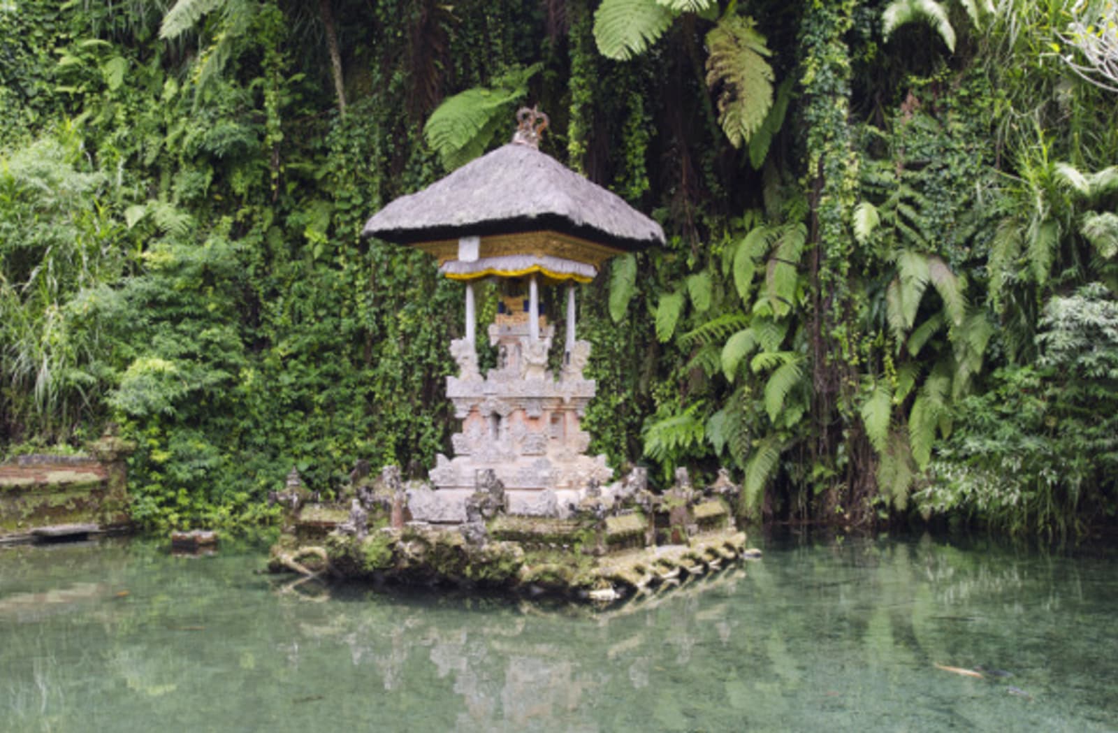 Small pagoda temple in a platform in a river, with jungle surrounding