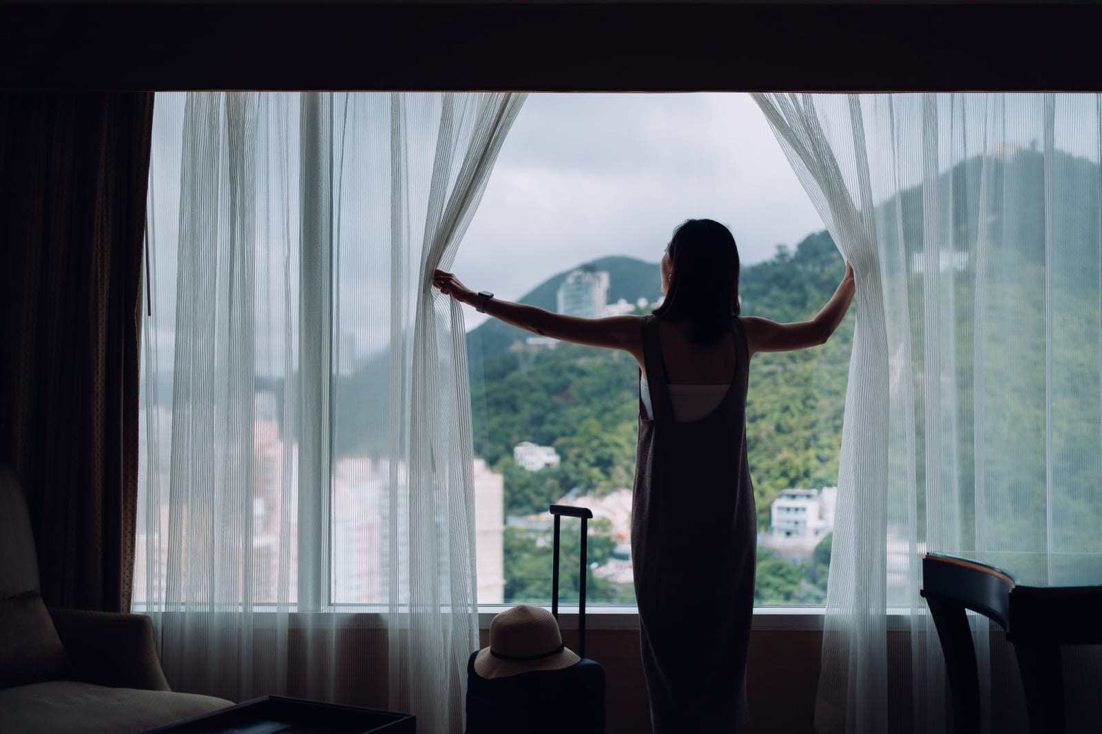 lady pushing apart curtains covering window in hotel room 