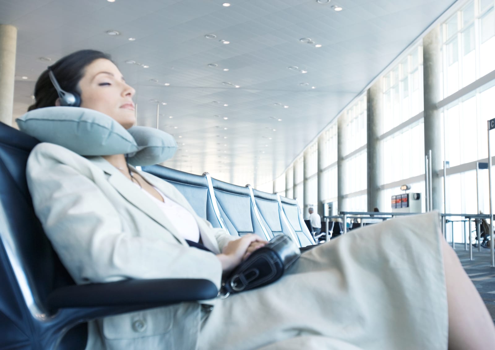 woman at airport resting head on a travel pillow