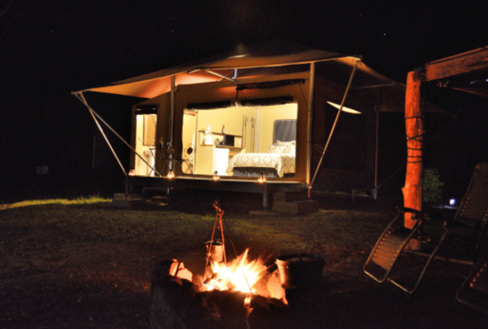 A bonfire in front of a glamping tent at night