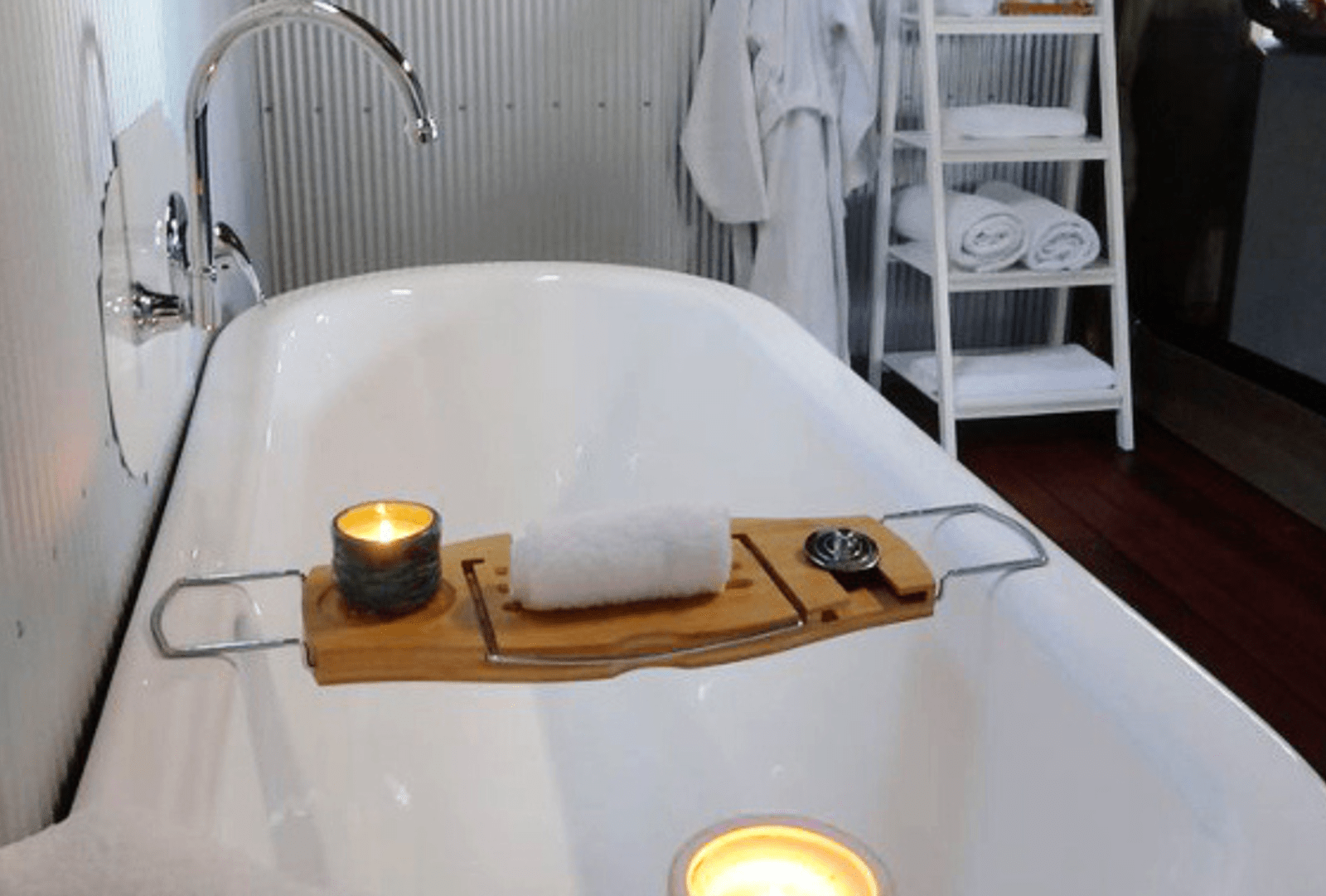 A bath tub with a tray on top filled with hot towel and scented candle