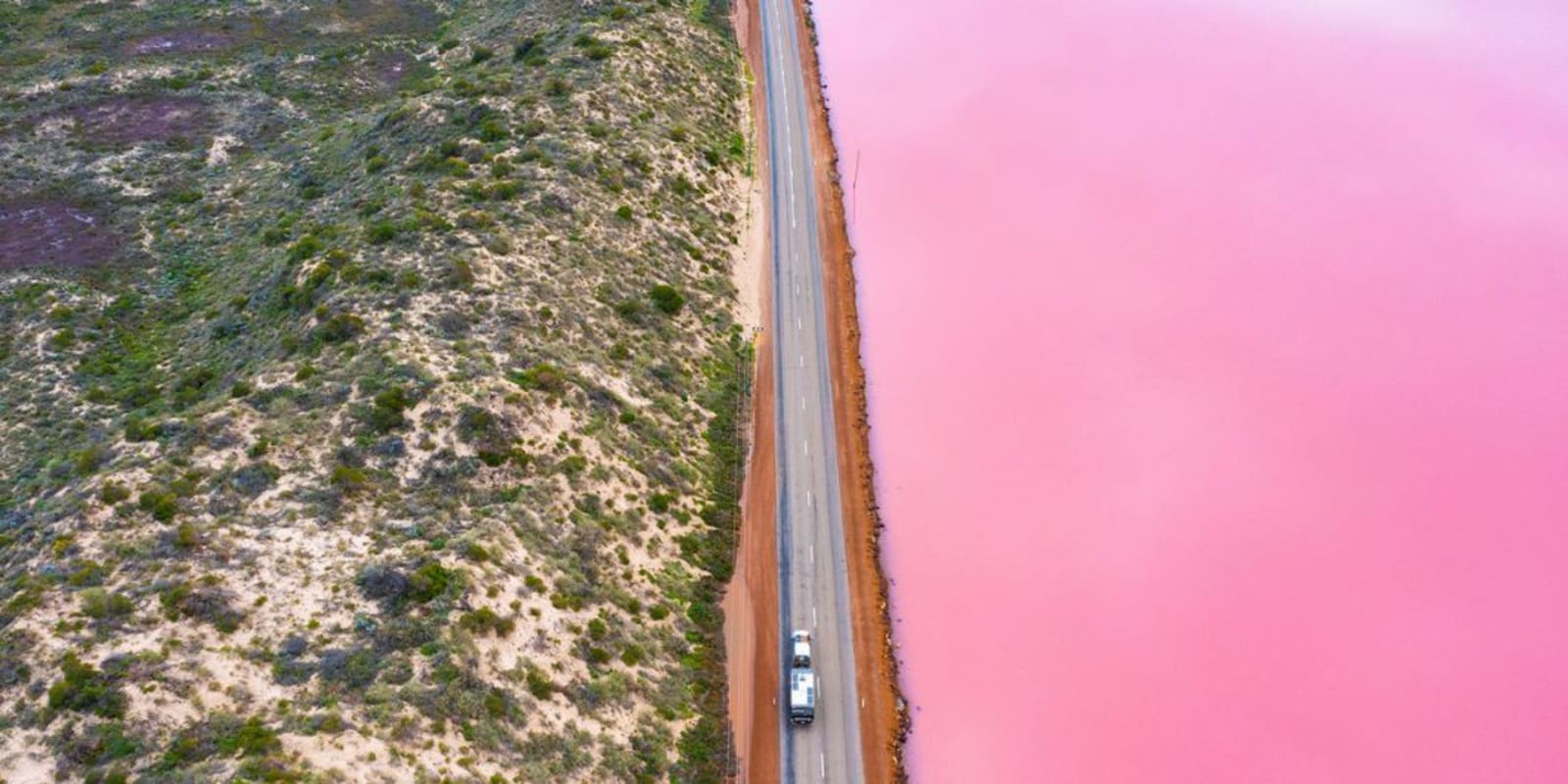 An aerial image of a car drive along a road past Hutt Lagoon which is a lovely pink colour