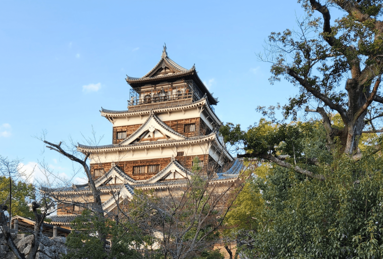 The large wooden Hiroshima Castle nestled among trees in the foreground