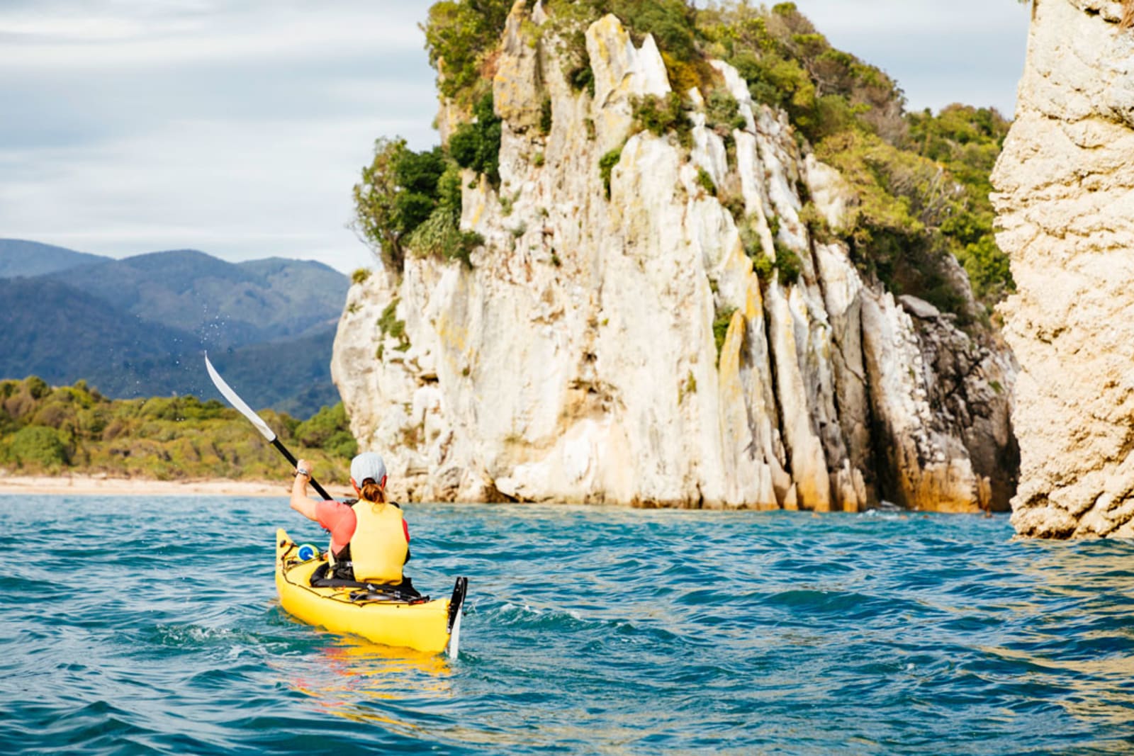 Woman kayaking beside Abel Tasman National Park cliffs 