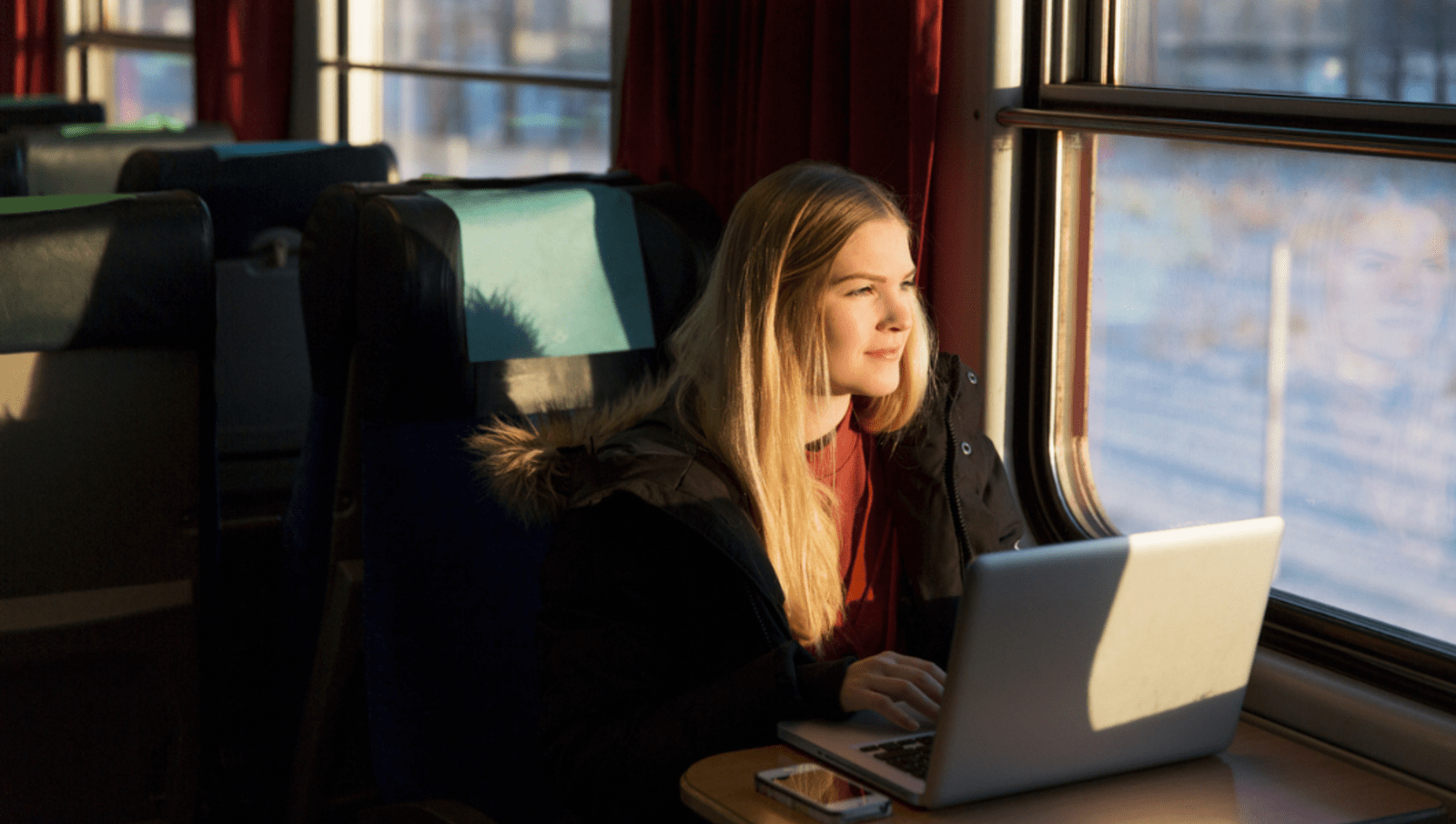 young lady looking out window on train with laptop open on table in front of her