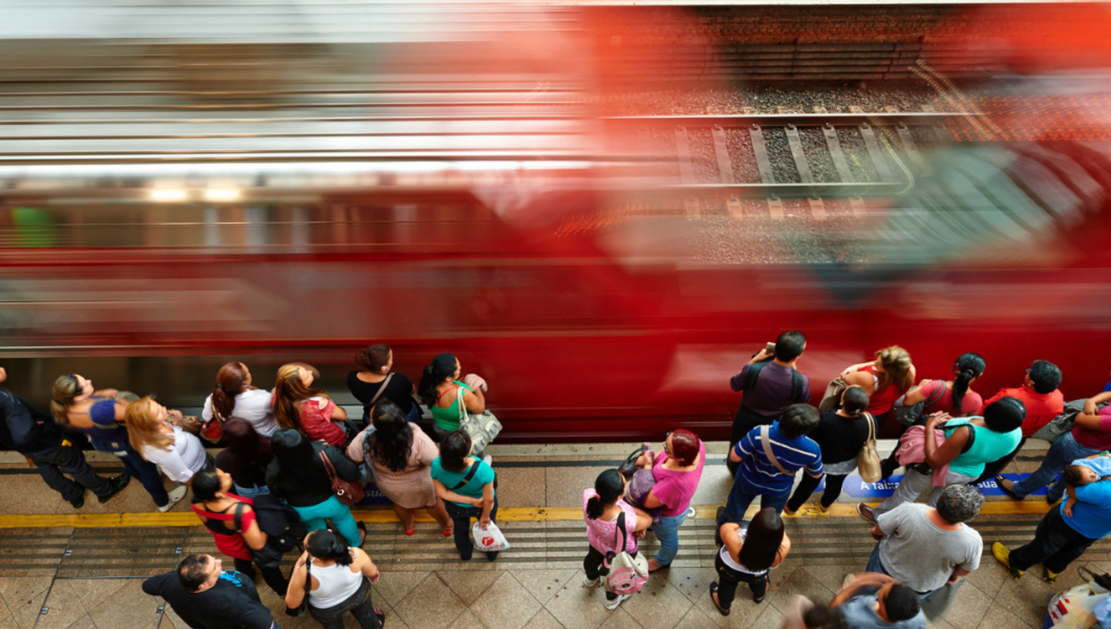 People standing on a train plaform as a red train drives past quickly