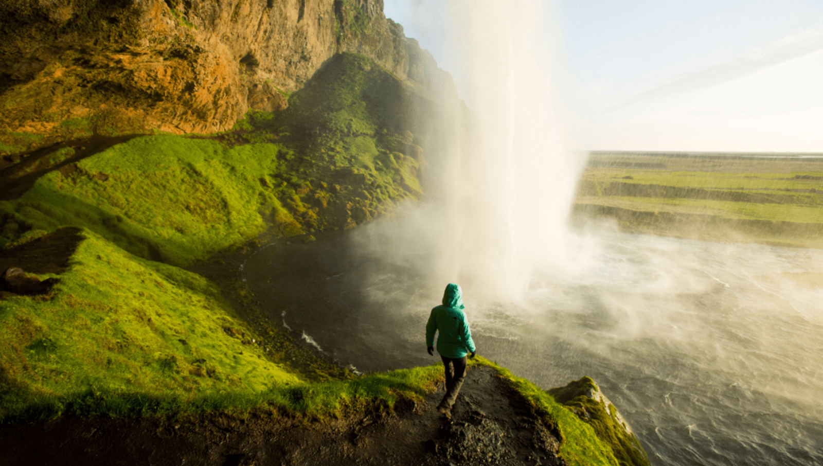 Lady walking down small cliff underneath waterfall