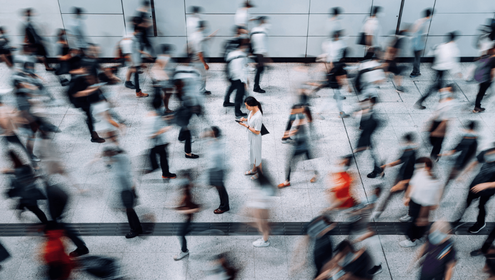 Lady standing still at busy station looking at her phone while everyone else moves fast 