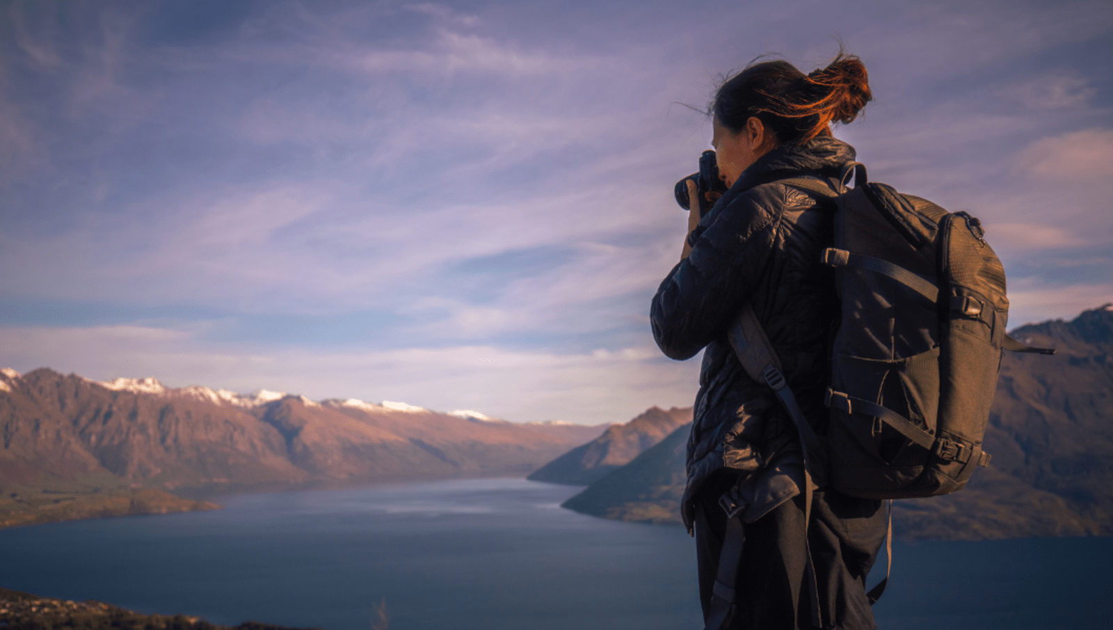 Lady taking a photo on top of a mountain overlooking other mountains