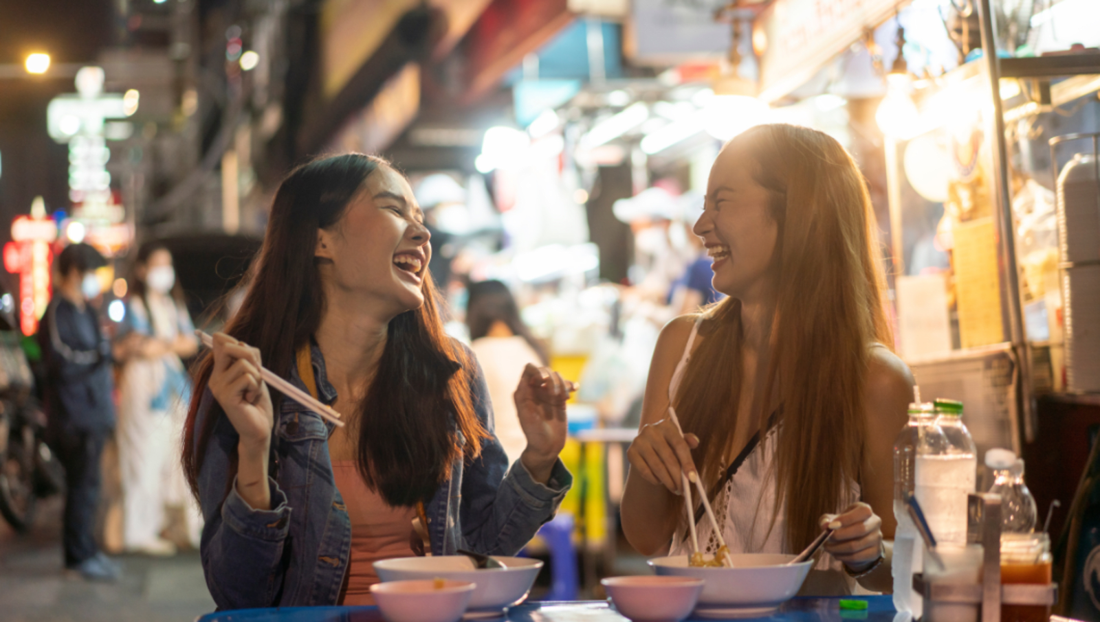 two friends laughing and eating noodles on street