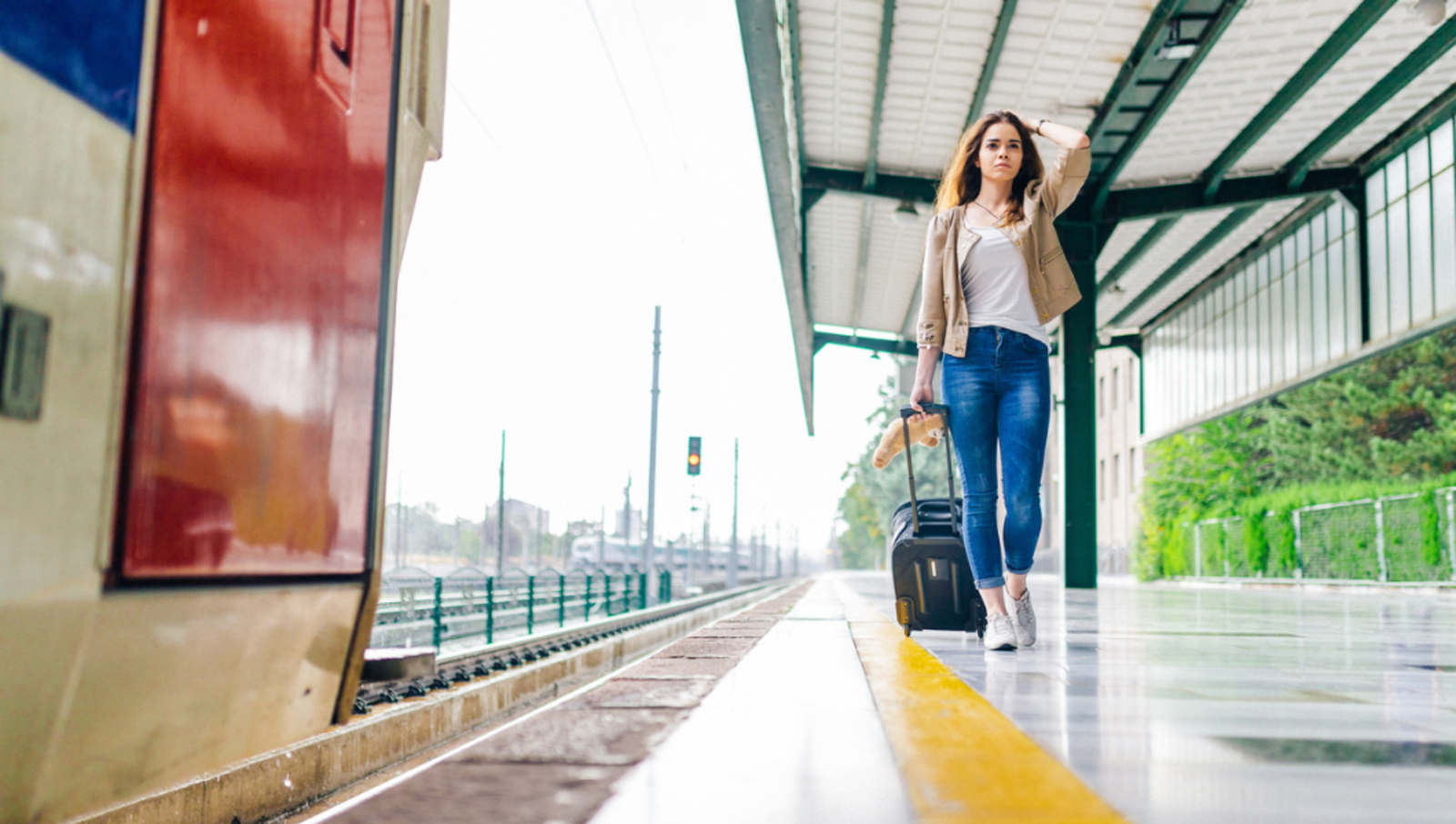 Lady pulling suitcase on train platform as end of train can be seen leaving the corner of the photo