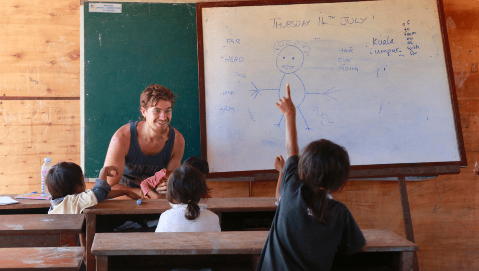 Man teaching to 3 young children with whiteboard with drawings in background