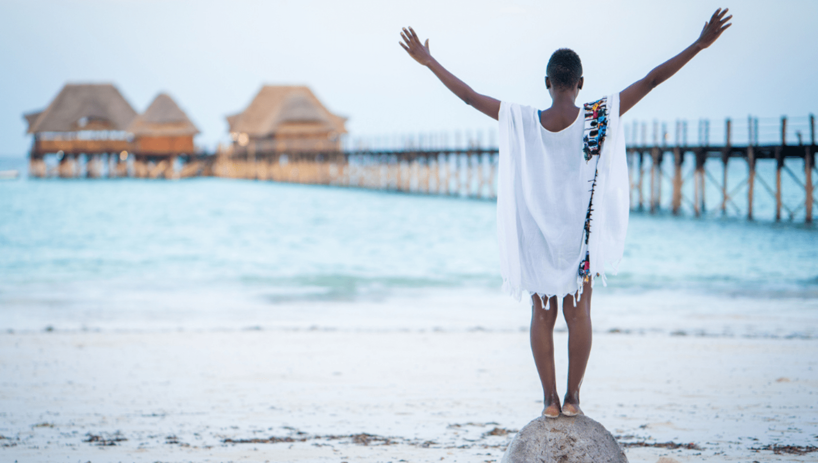 lady standing on rock with arms out on beach 