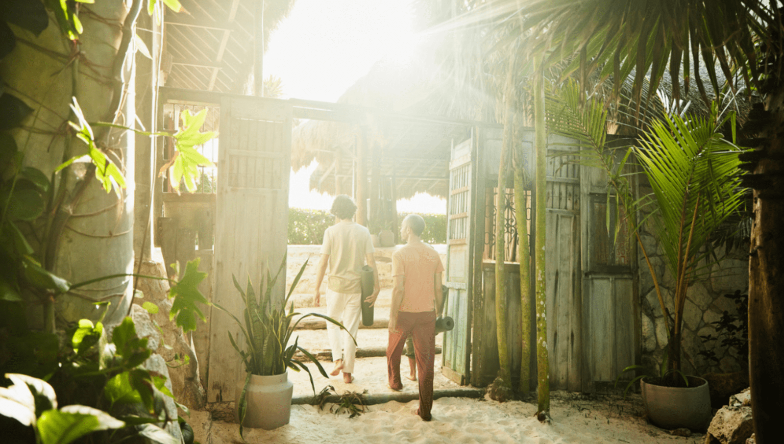 couple walking through doors of an eco hotel holding yoga mats