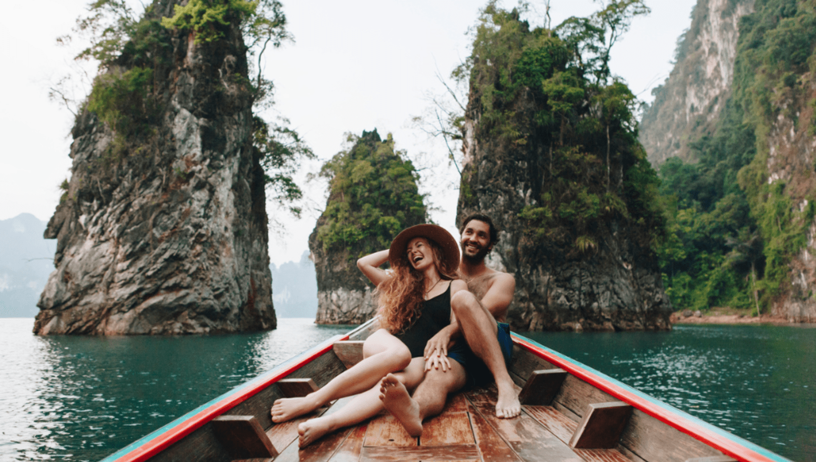 Couple sitting at top of boat with large rock formations in background on blue water
