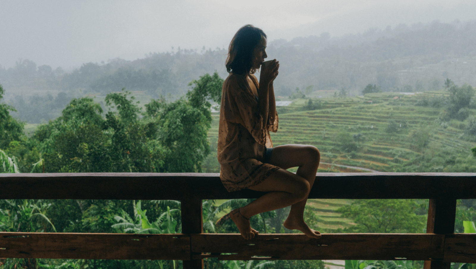 Lady sitting on balcony overlooking rainy rice terrace while sipping on tea