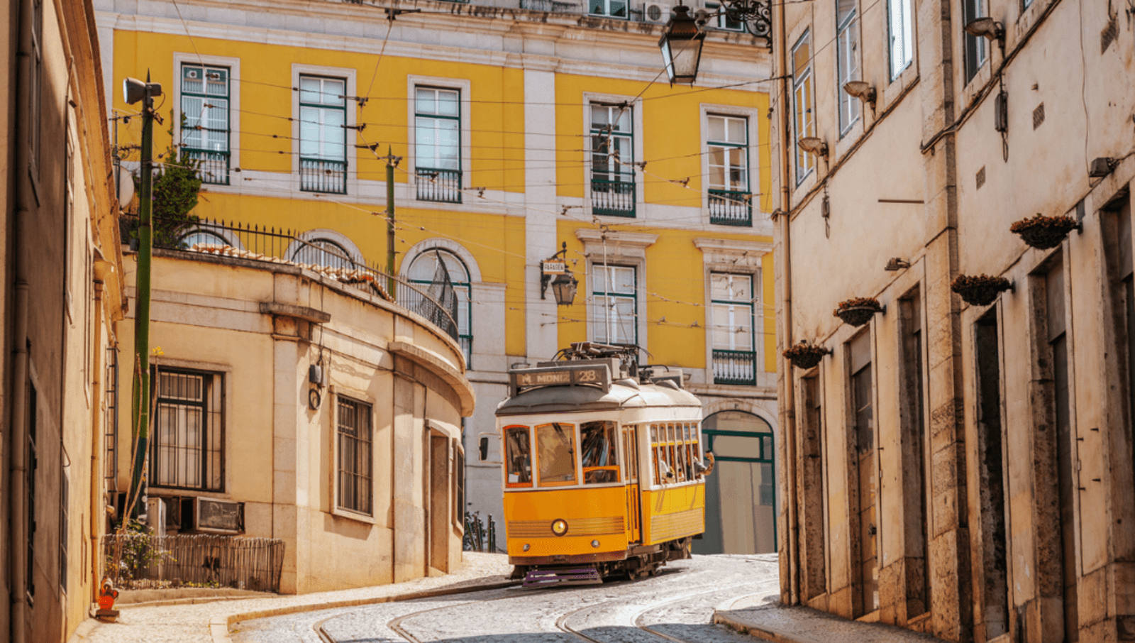 Yellow tram travelling down a small street lined with tall buildings