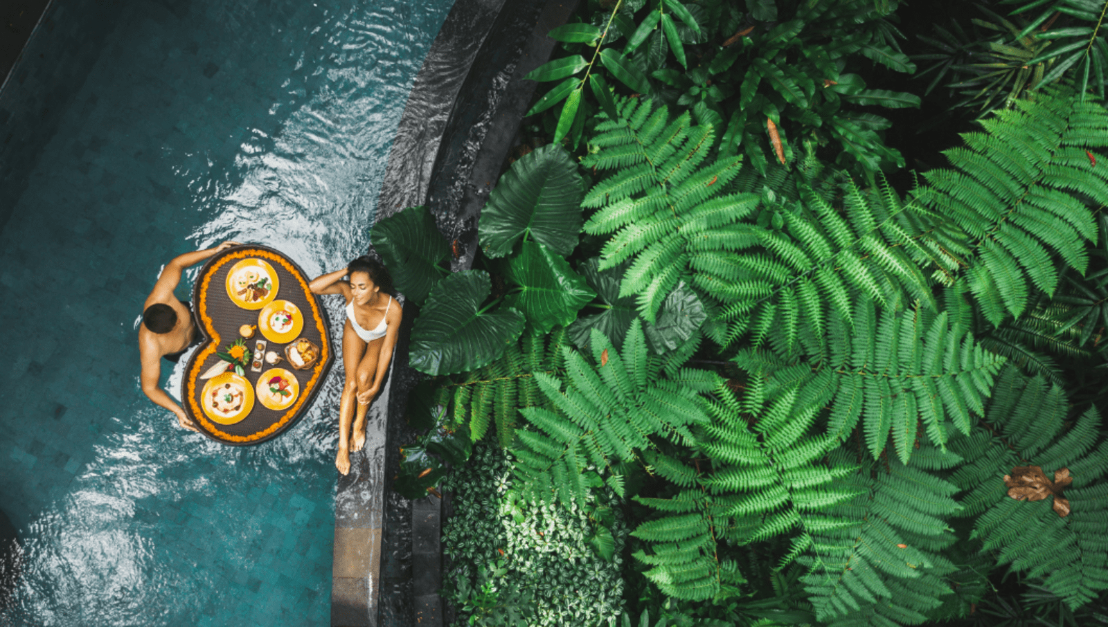 Couple in pool with lush garden with a floating tray full of food in pool