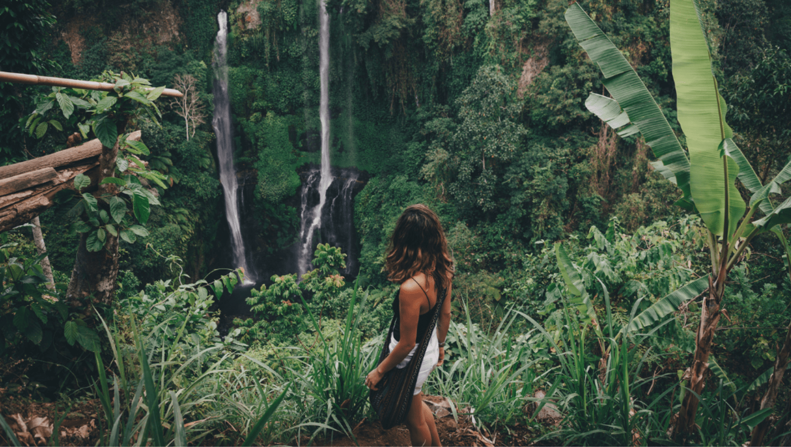 Girl standing on cliff facing forest with waterfalls