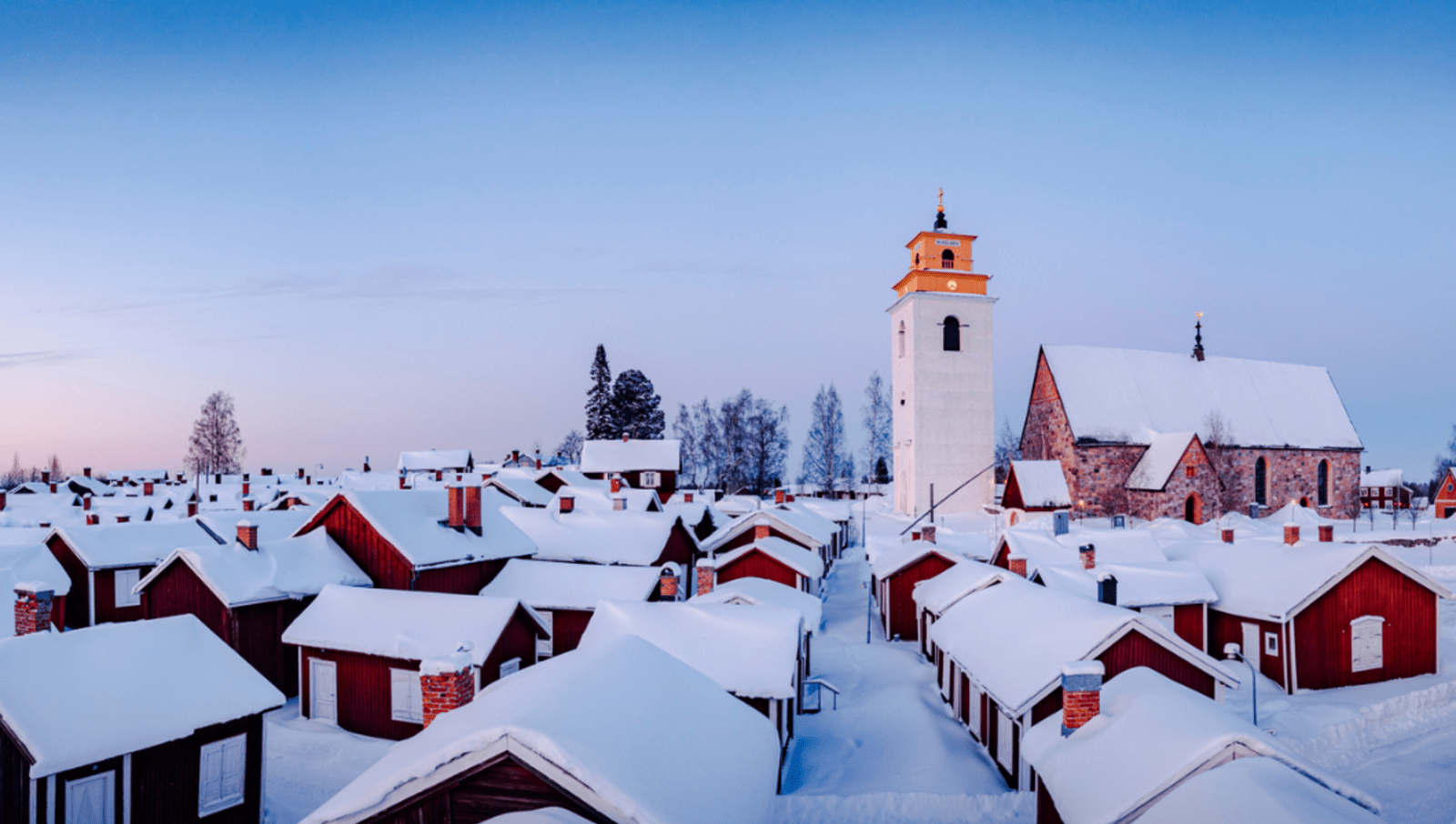 Small red houses covered in blanket of thick snow with tall church tower in middle