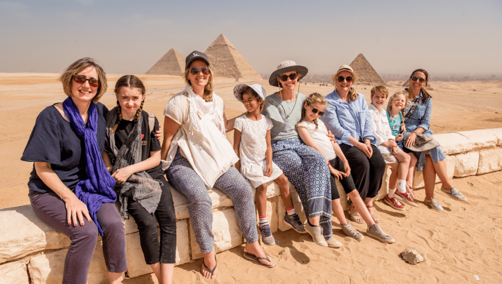Mothers and daughters sitting along bricks in front of pyramids