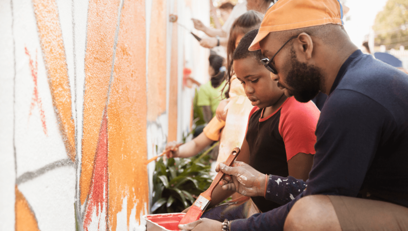man and young boy painting art on wall with orange paint