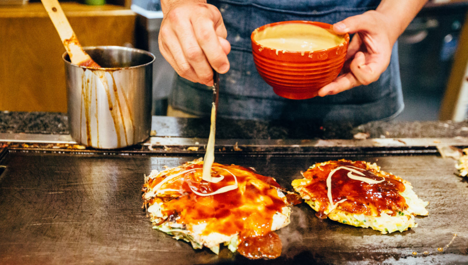 Man using spoon to poor sauce on okonomiyaki pancake 
