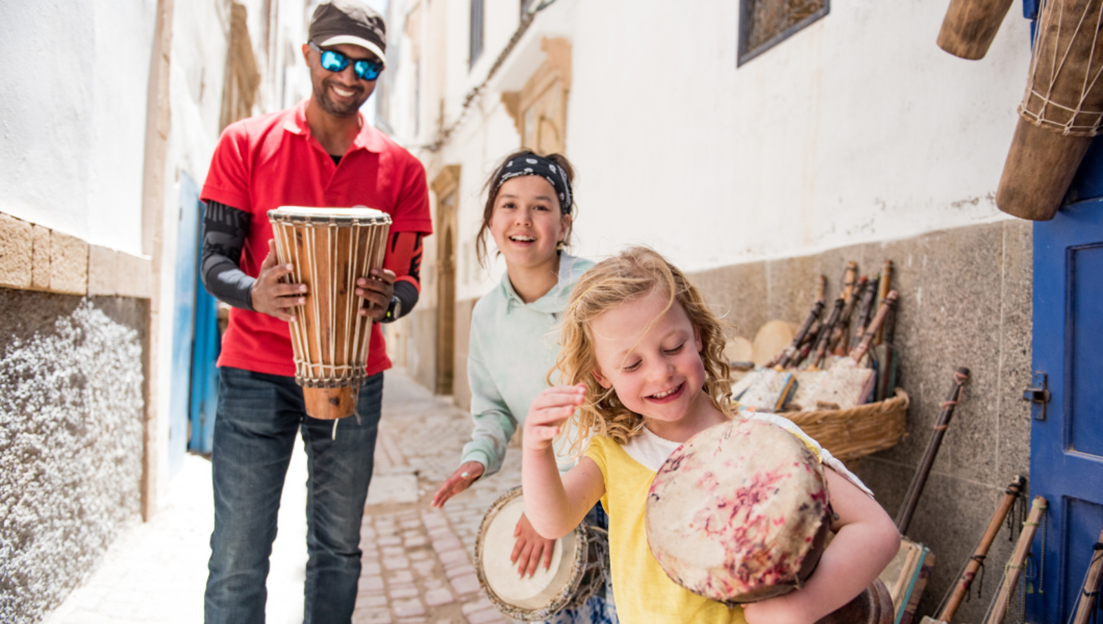 Man holding drum watching two younger girls play drums