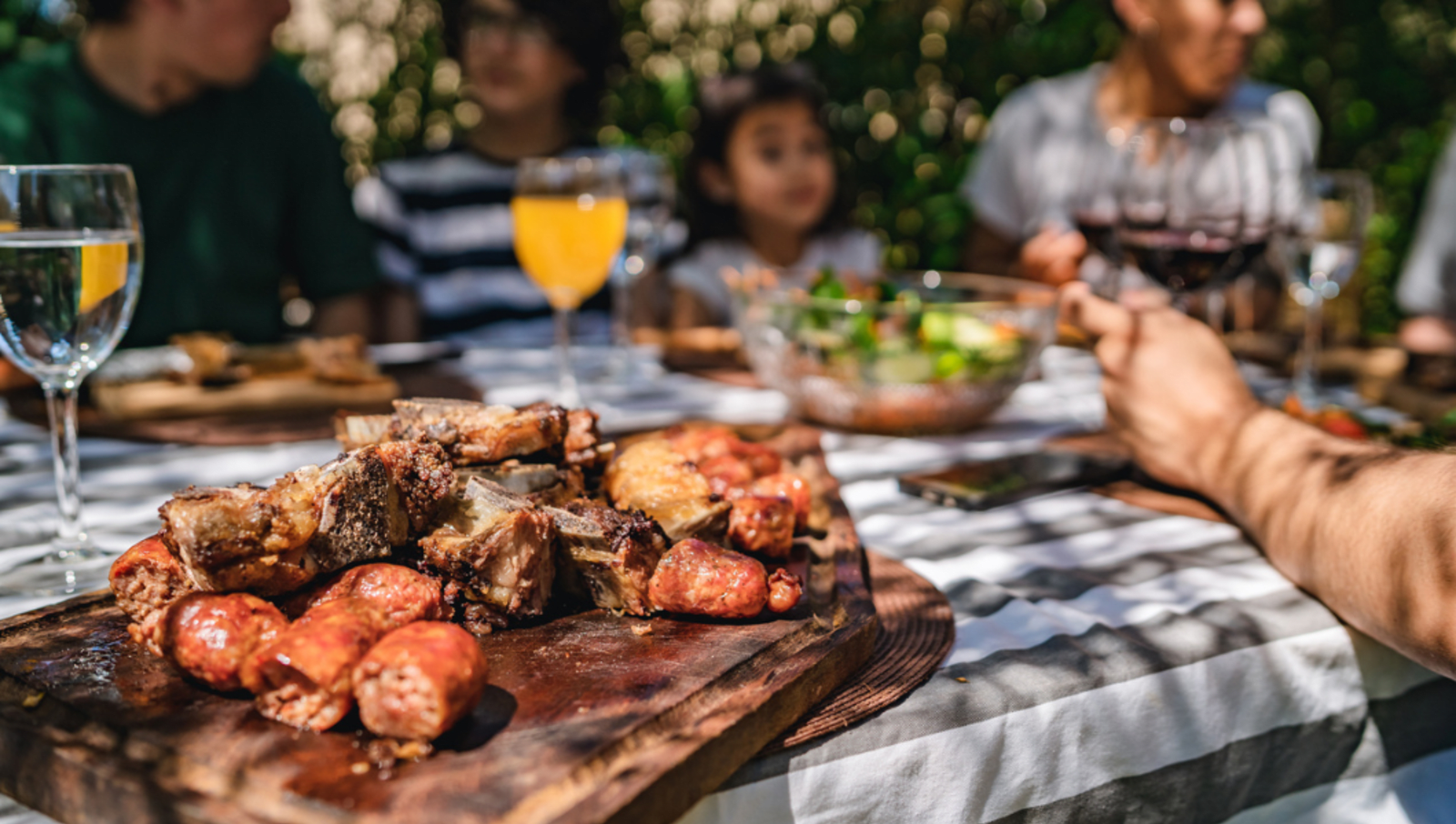 Grilled meat on a board on table with family sitting around