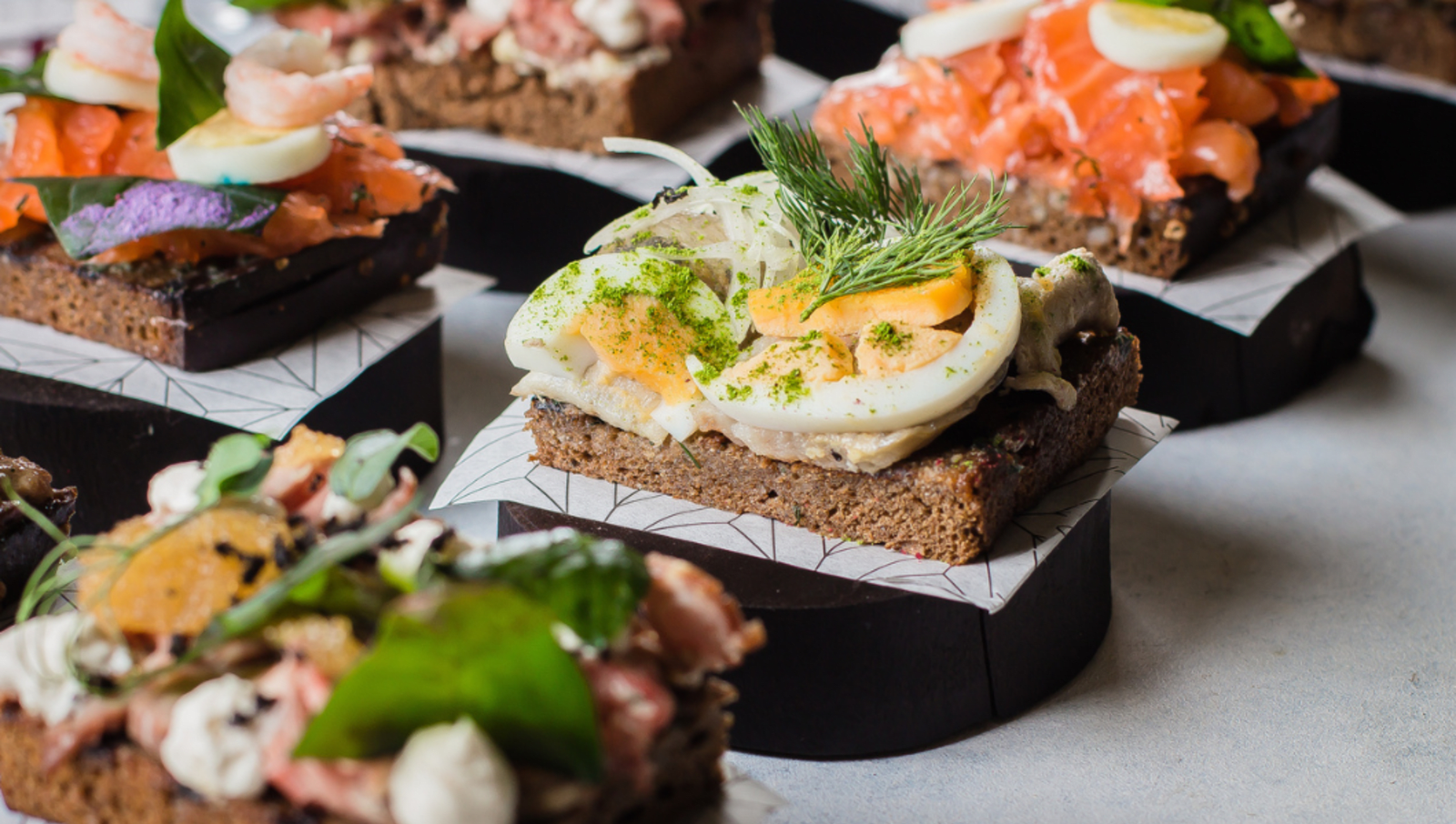 Open style sandwiches lined up sitting on tall wooden plates