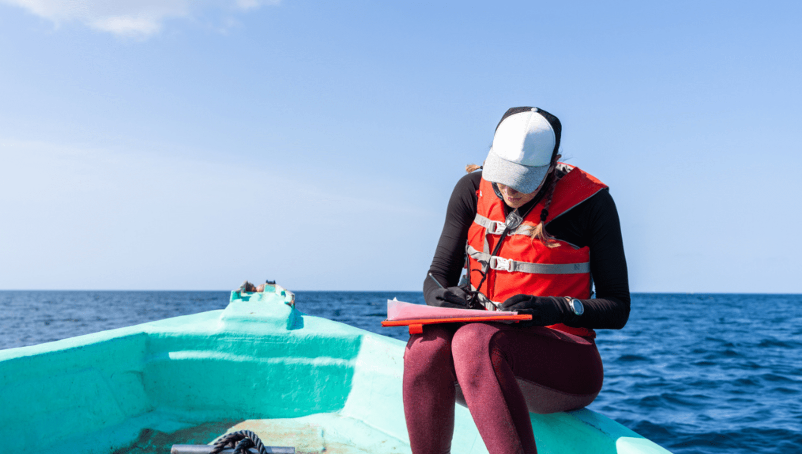 lady sitting on edge of blue boat writing notes on clipboard