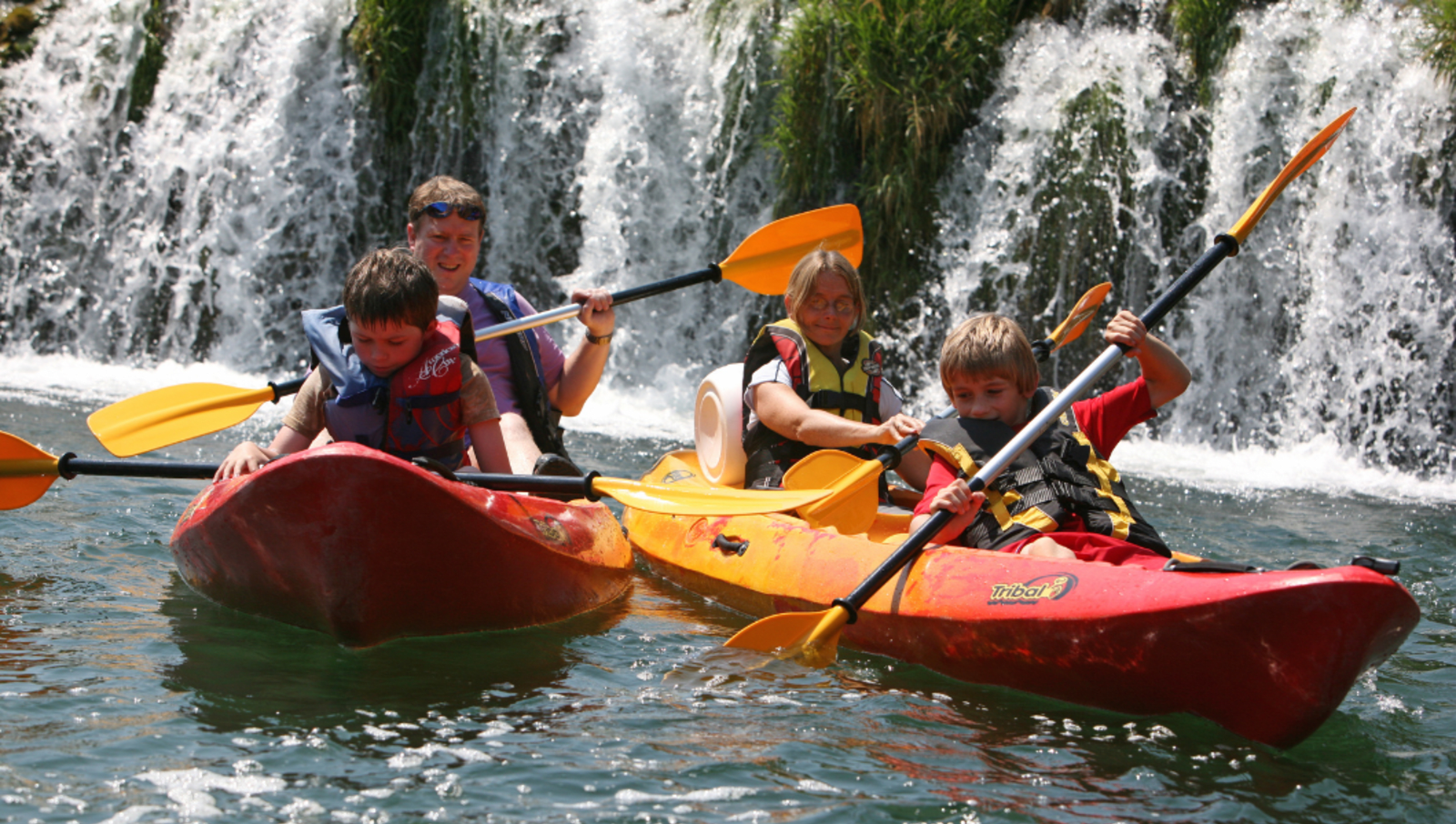 family kayaking in front of waterfall