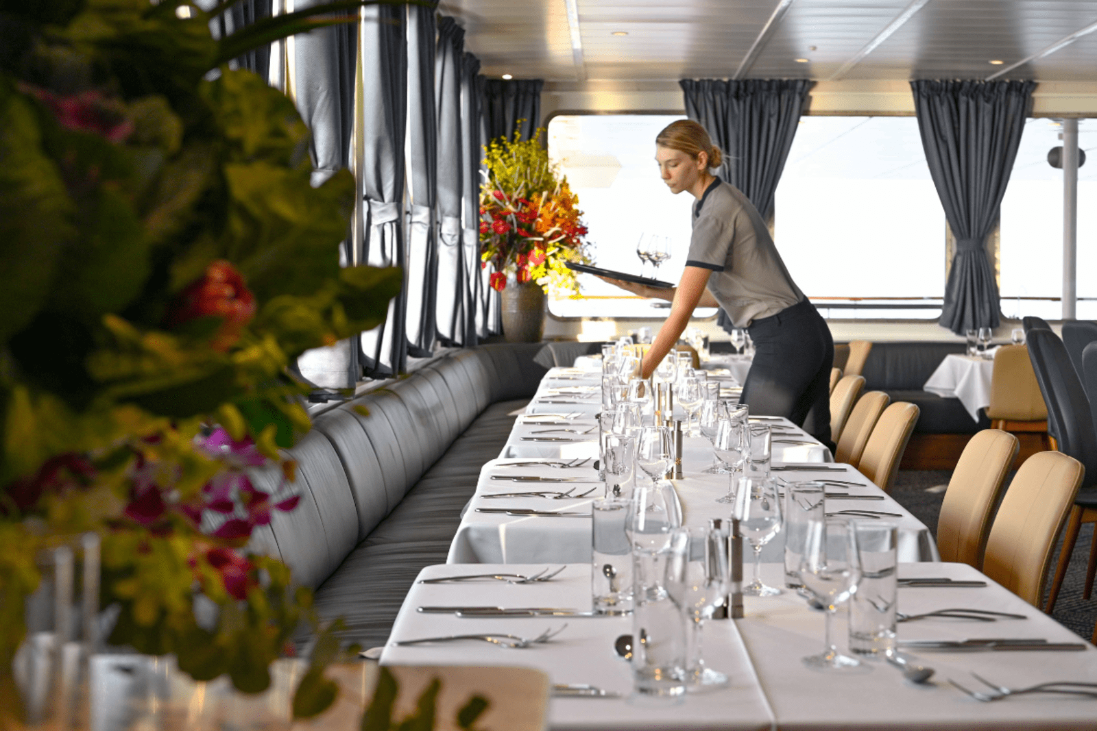 A woman sets places at a dining tables aboard a small cruise ship