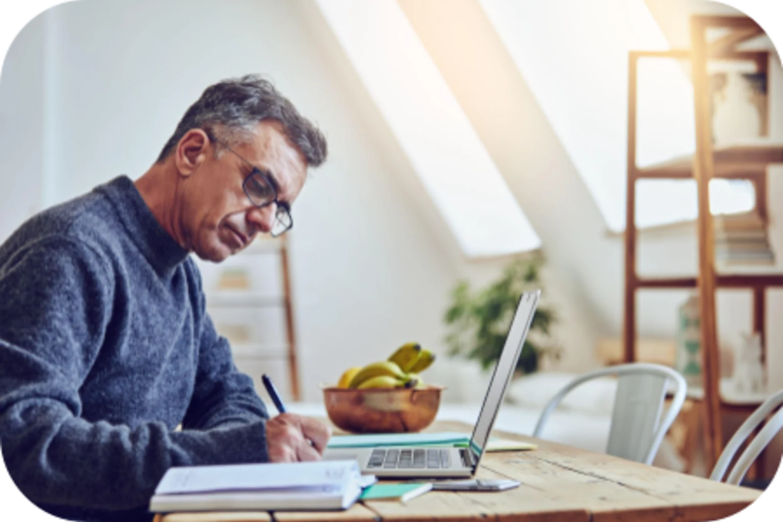 Middle-aged man writing in front of a laptop in a bright study