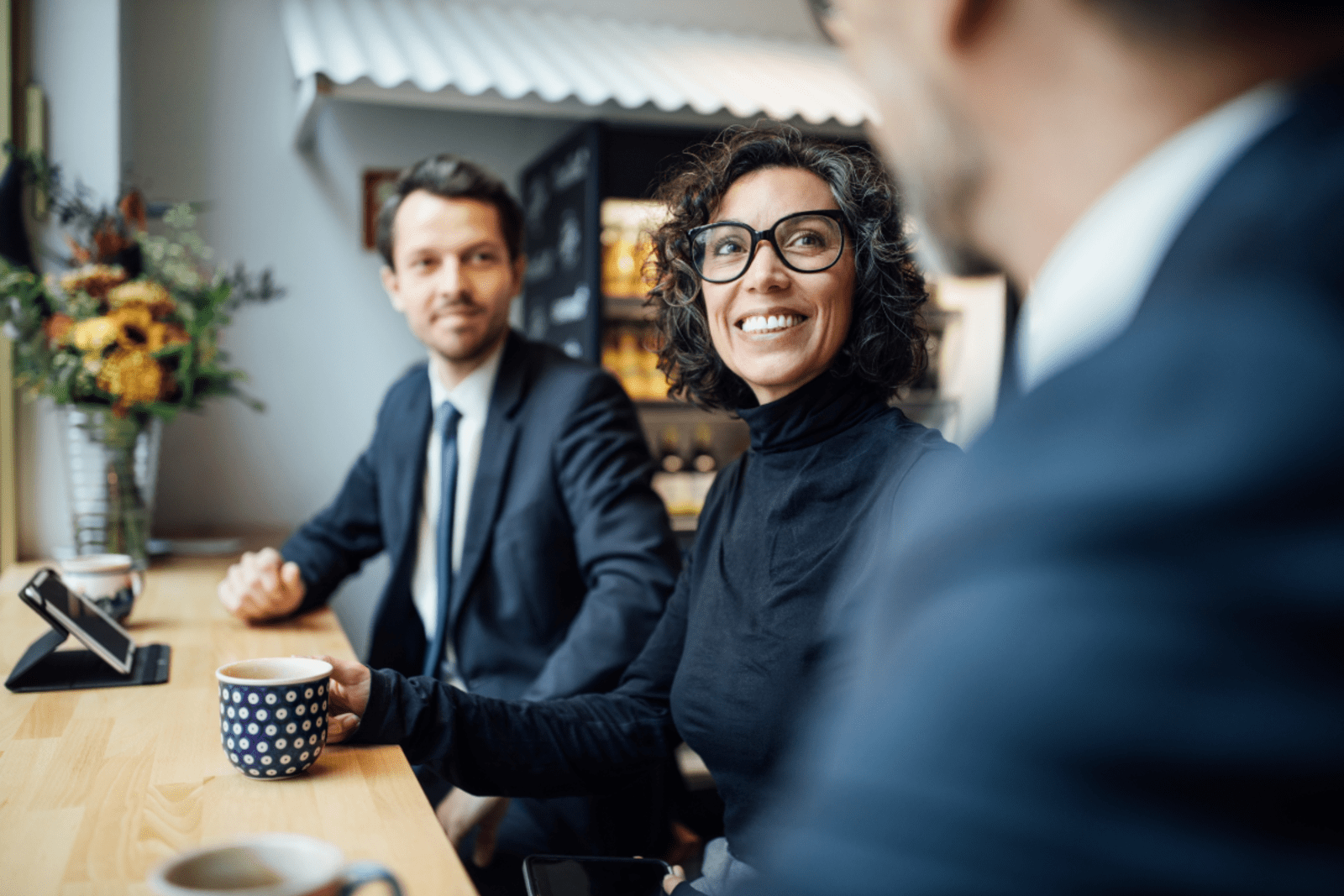 three business people facing each other at a coffee shop with a cup of coffee in one hand