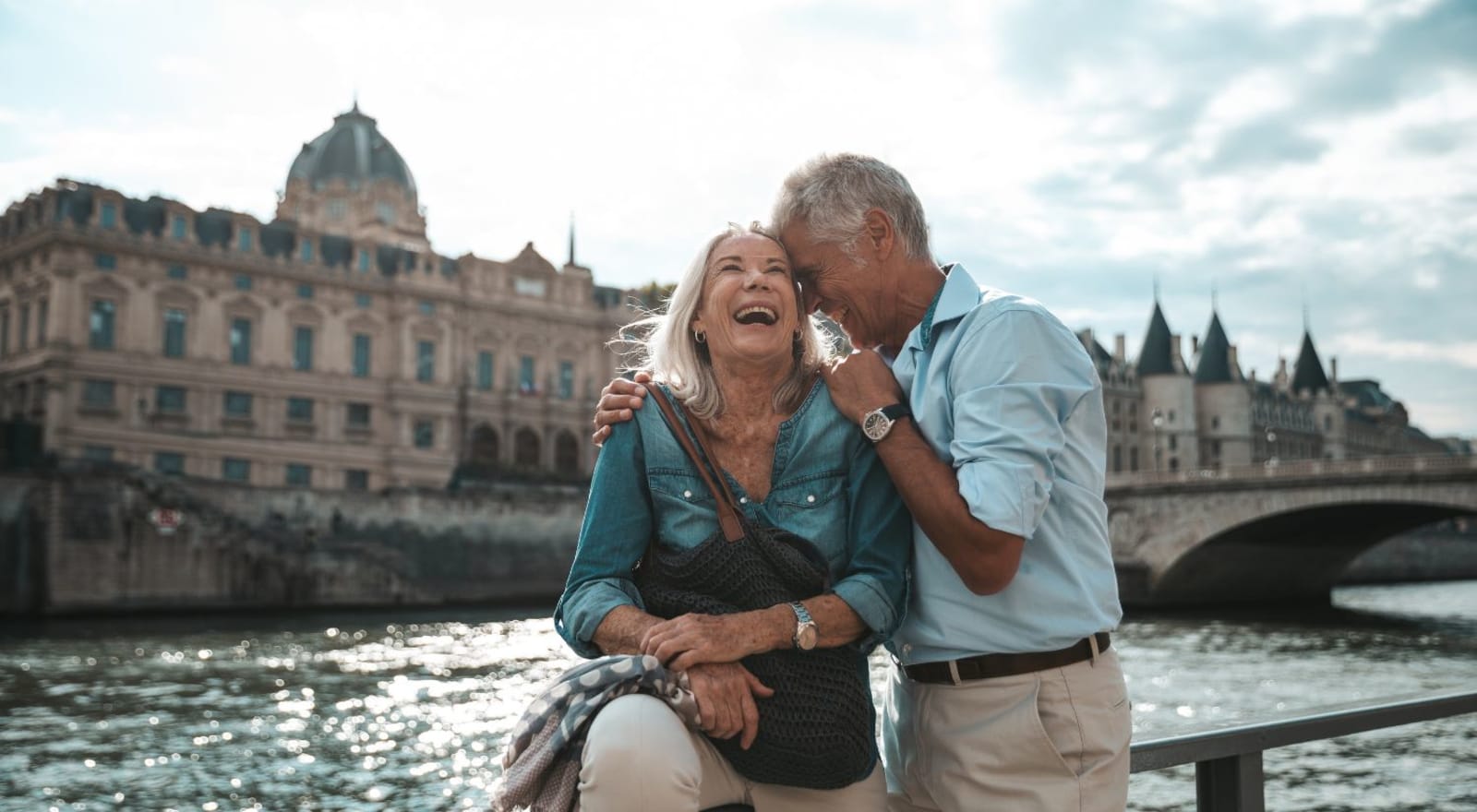 senior couple laughing and sitting beside river in paris