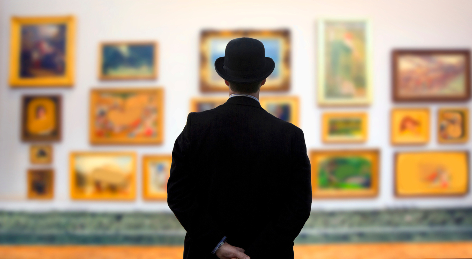 man wearing suit and hat staring at pictures in art gallery