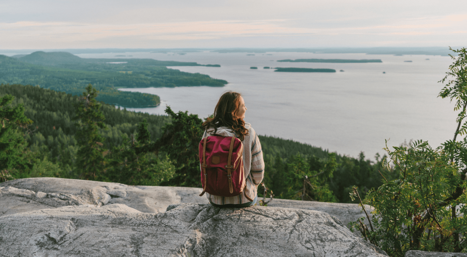 lady sitting on rock overlooking forest and lake in Finland