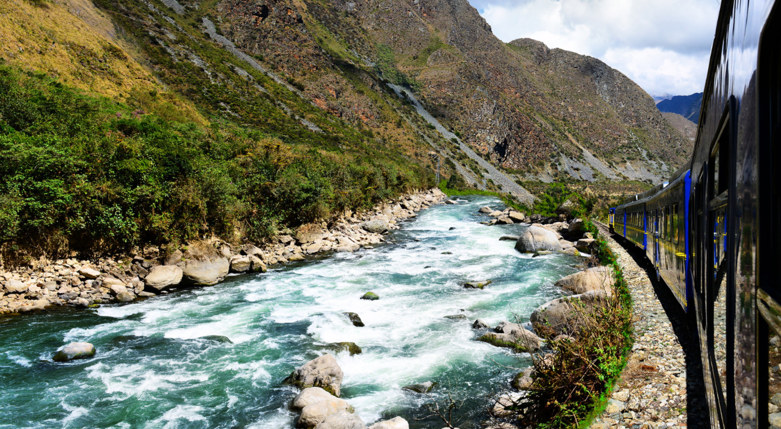 train riding past river by the side of a mountain in peru