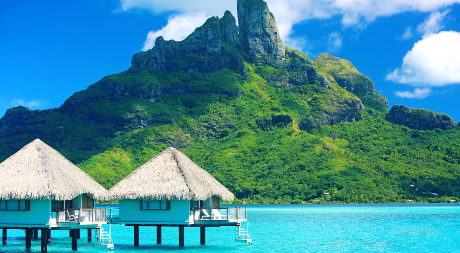 overwater villas in bora bora with tall rocky mountain in background