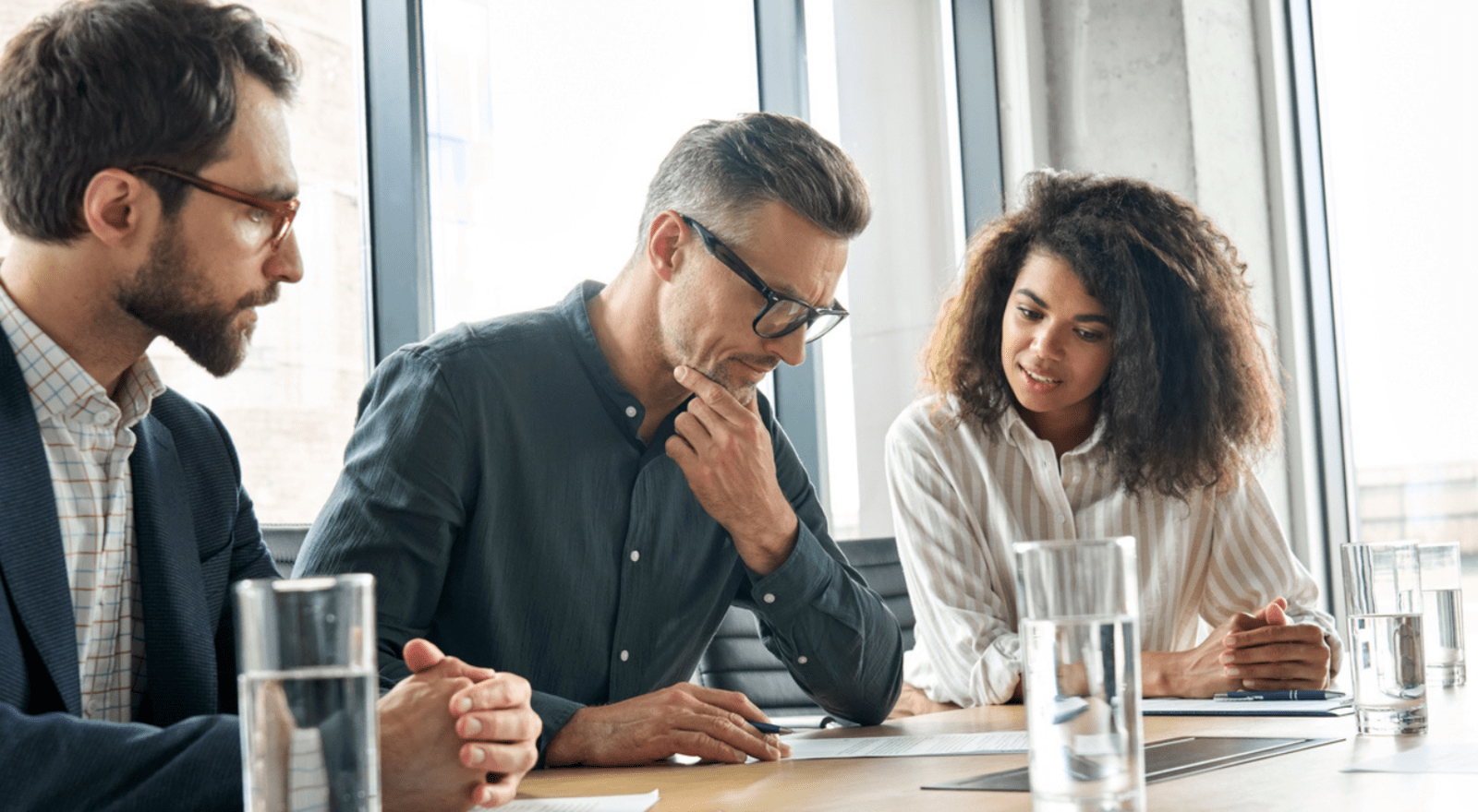 three business people sitting at a table reading a document