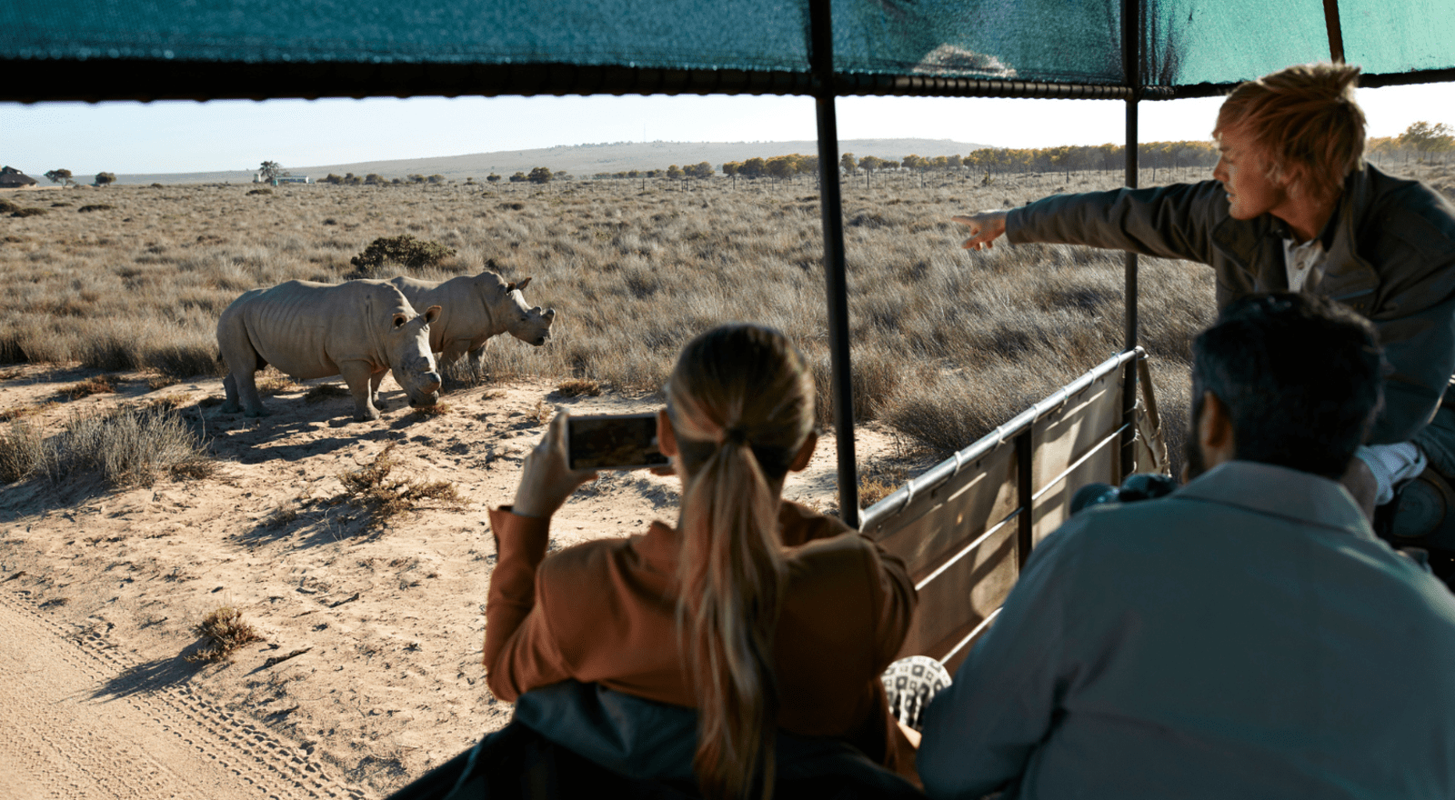 couple sitting in safari car while guide points to rhinoceres in south africa