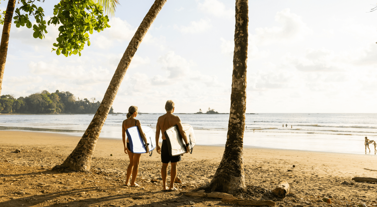 older couple holding boogie boards on beach of costa rica