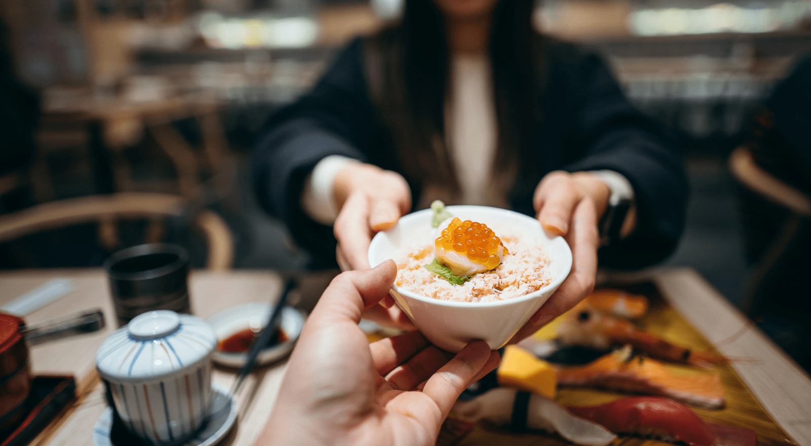 man and woman passing bowl of seafood to each other across table in japan