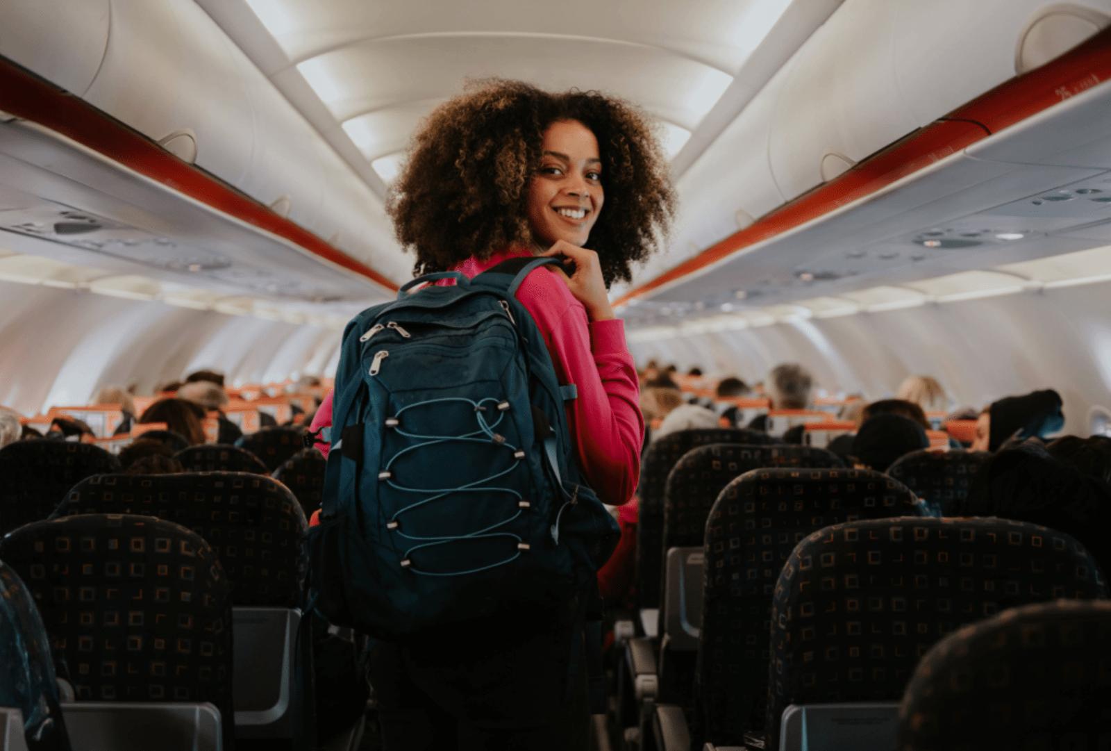 A happy solo woman traveller walks down the aisle inside a plane