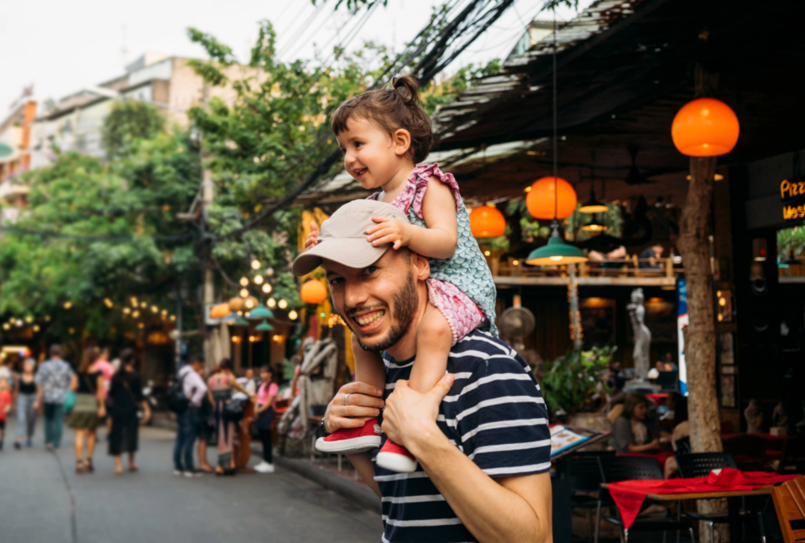 A man carries his young daughter on his shoulders in an outdoor market