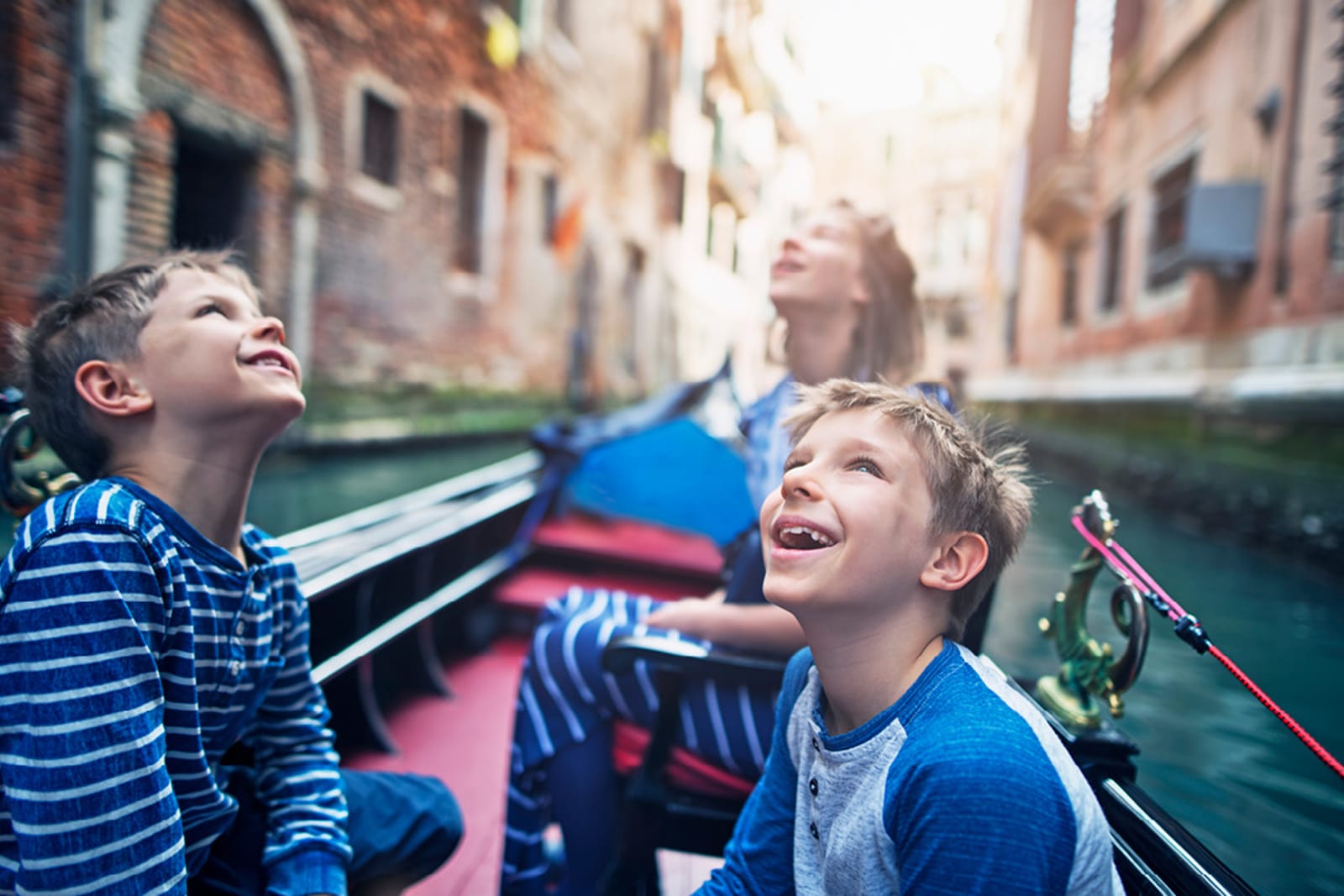 Three young kids marvelling at the scenery while riding a gondola in Venice
