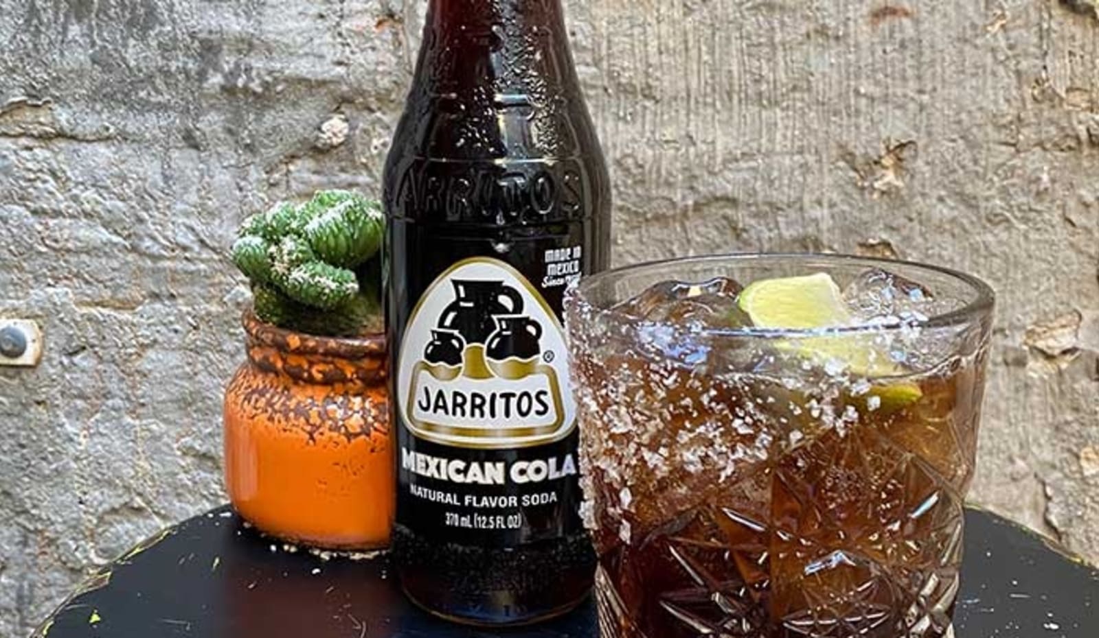 A glass of Charro Negro on a table next to a bottle of Jarritos Mexican Cola