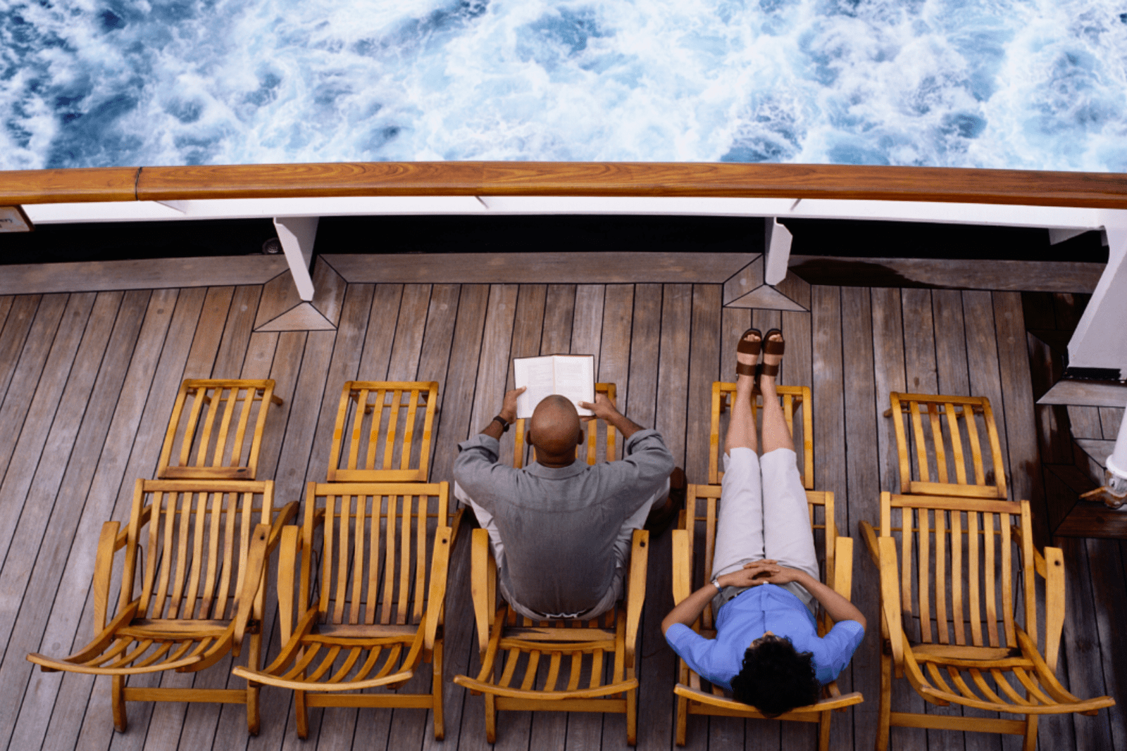 Two passengers relaxing on the deck of a cruise ship; one of them is reading a book